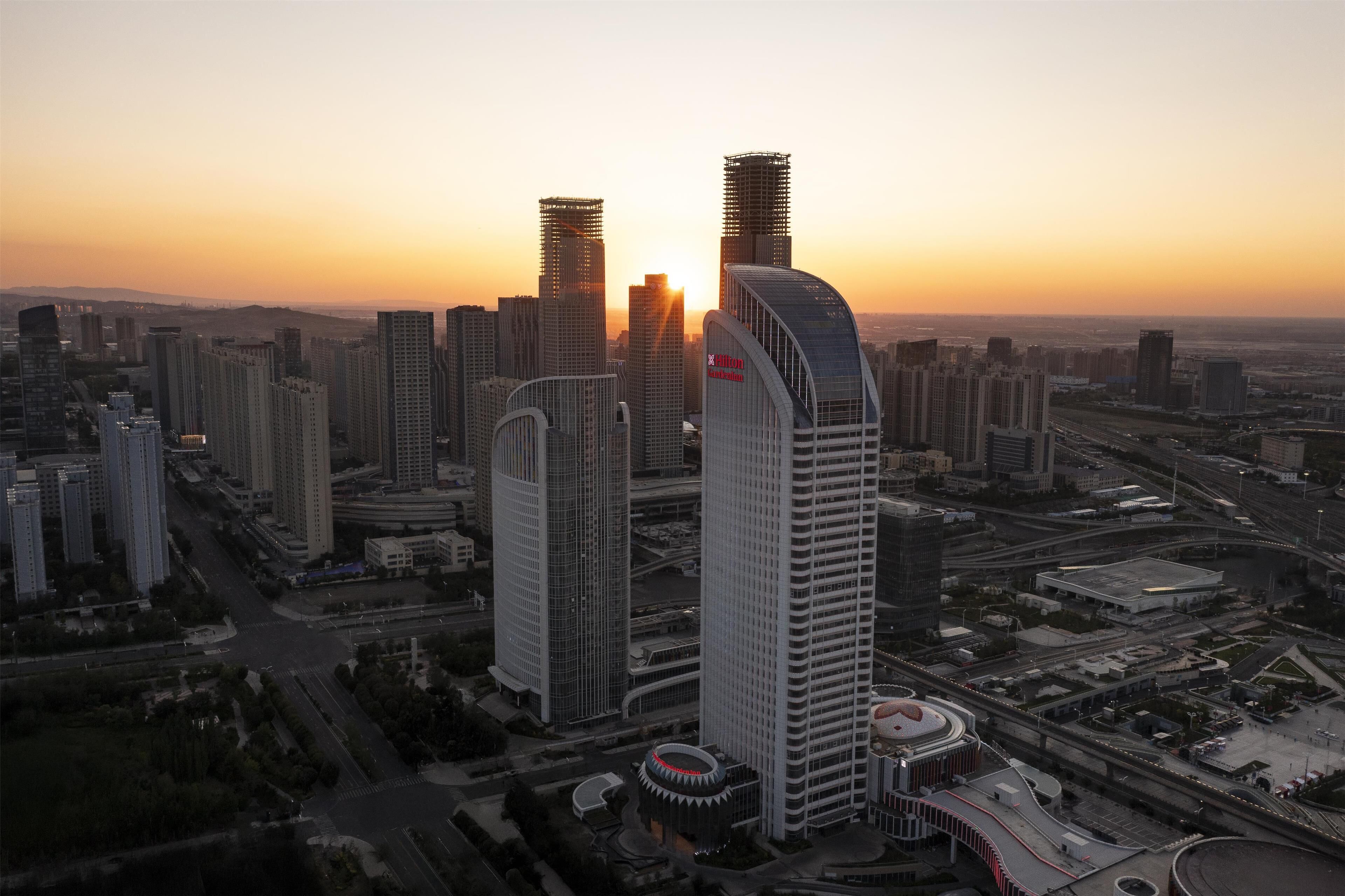 A cityscape with high-rise buildings, a prominent curved skyscraper, and a circular structure with a dome.