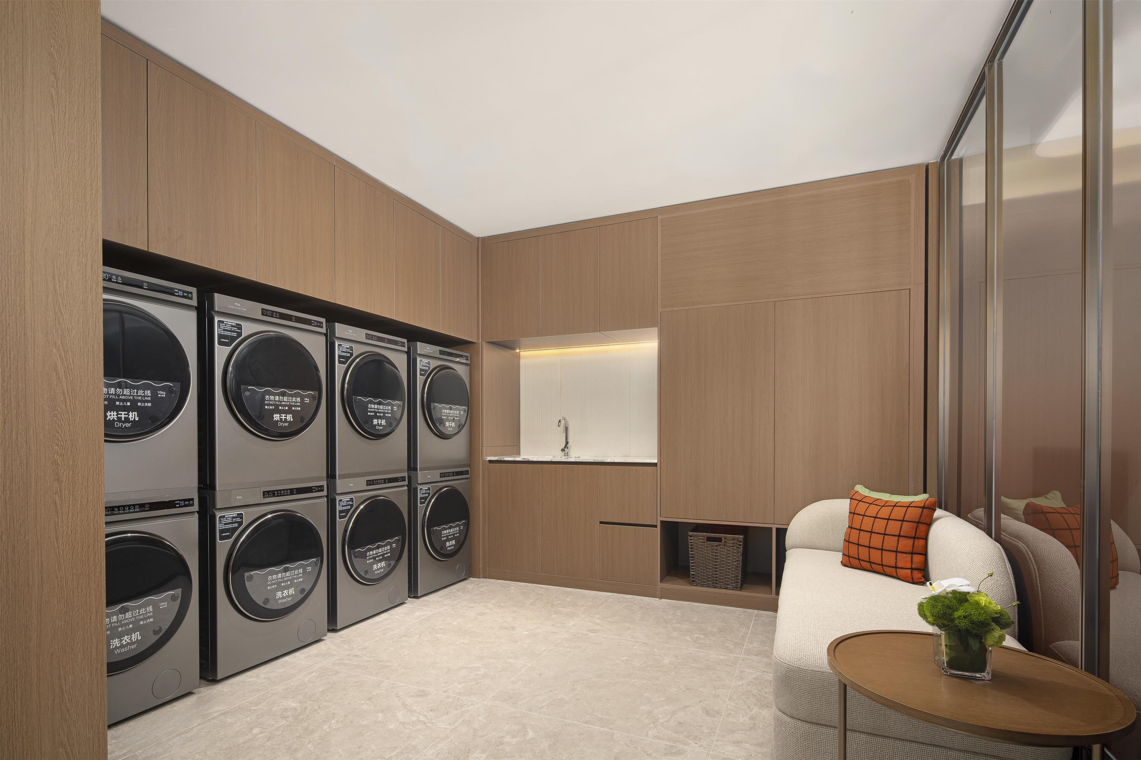 Un moderno cuarto de lavandería con varias lavadoras, un lavamanos y una zona de estar con un sofá y una mesita.