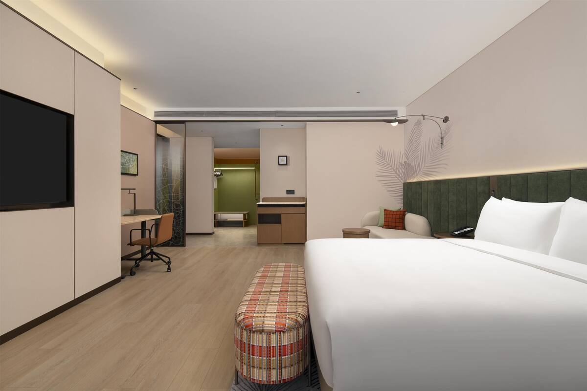 A modern hotel room with a large bed, a desk, a chair, and a small table.