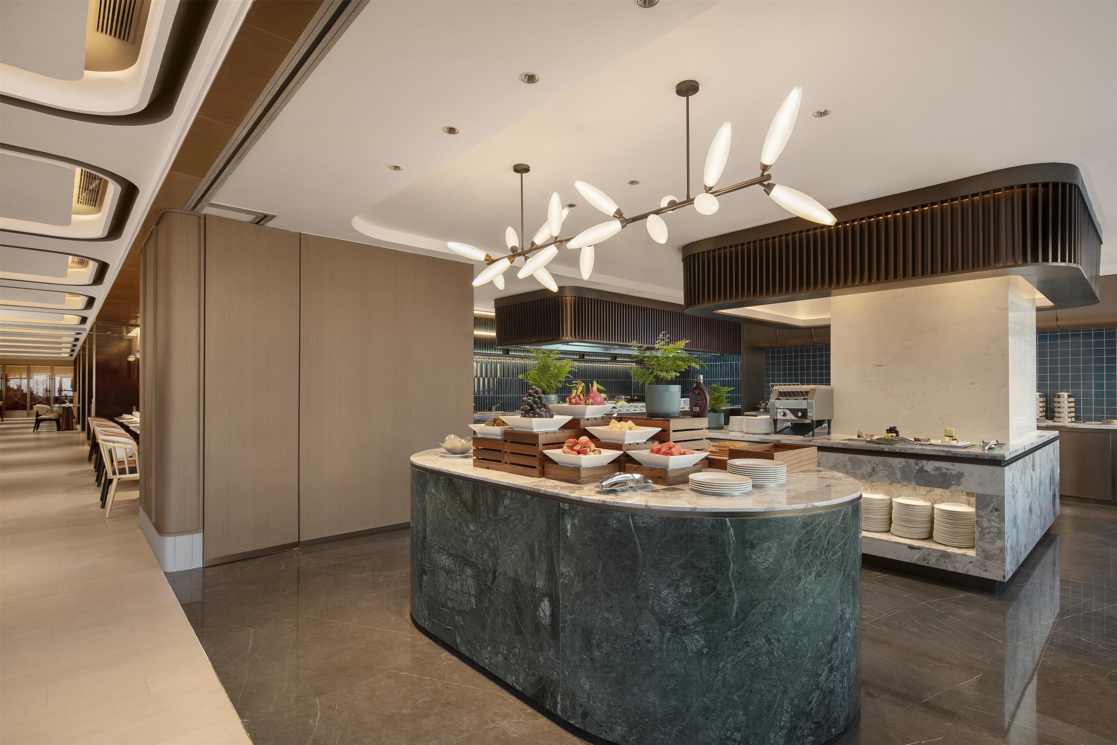 A modern hotel lobby with a marble reception desk, a ceiling fan, and a buffet area.