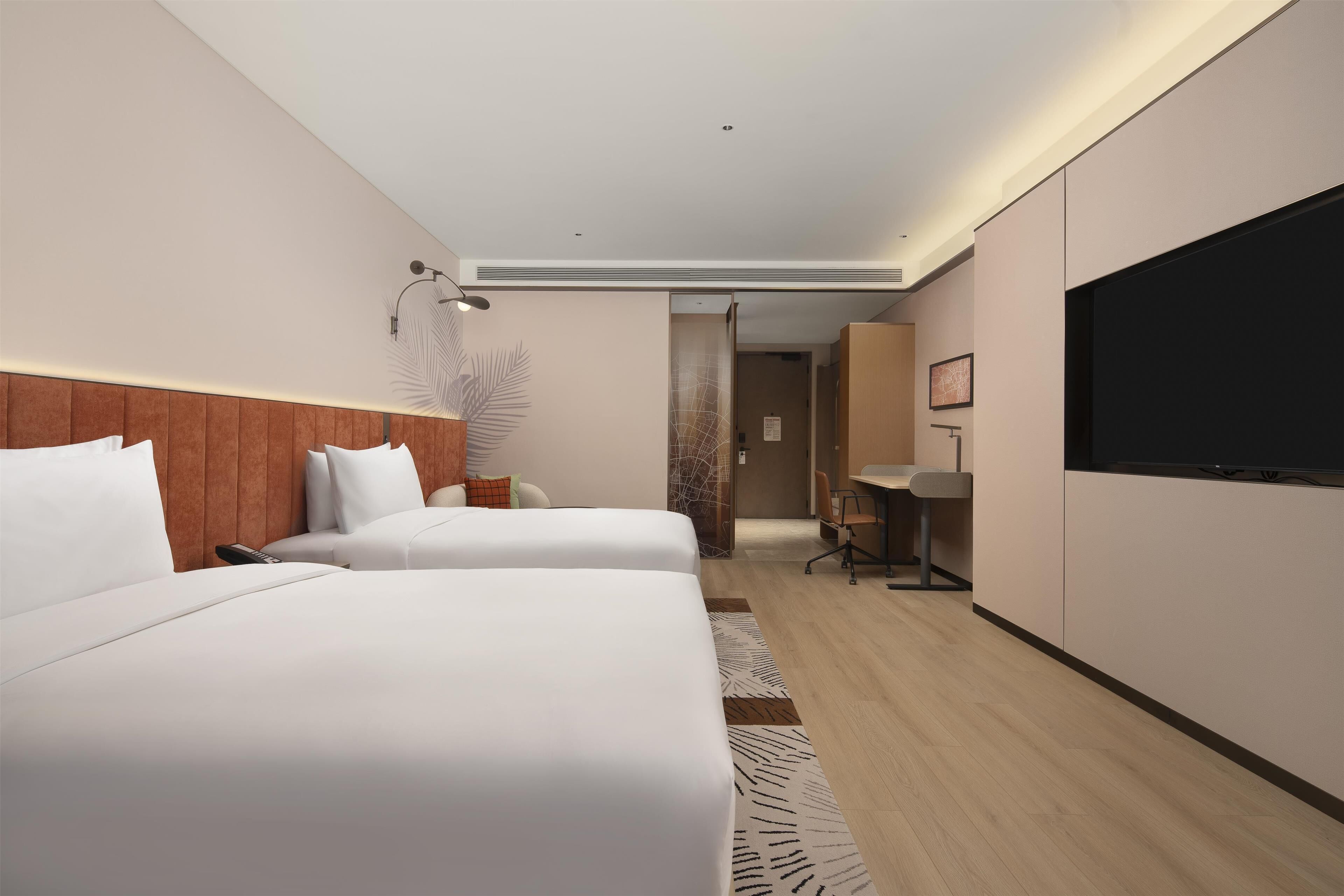 Habitación de hotel con dos camas, un escritorio, una silla, un televisor y una puerta que da a otra habitación.