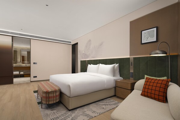 Una habitación de hotel moderna con una cama grande, una mesita de noche, un sofá, una alfombra estampada y un espejo.