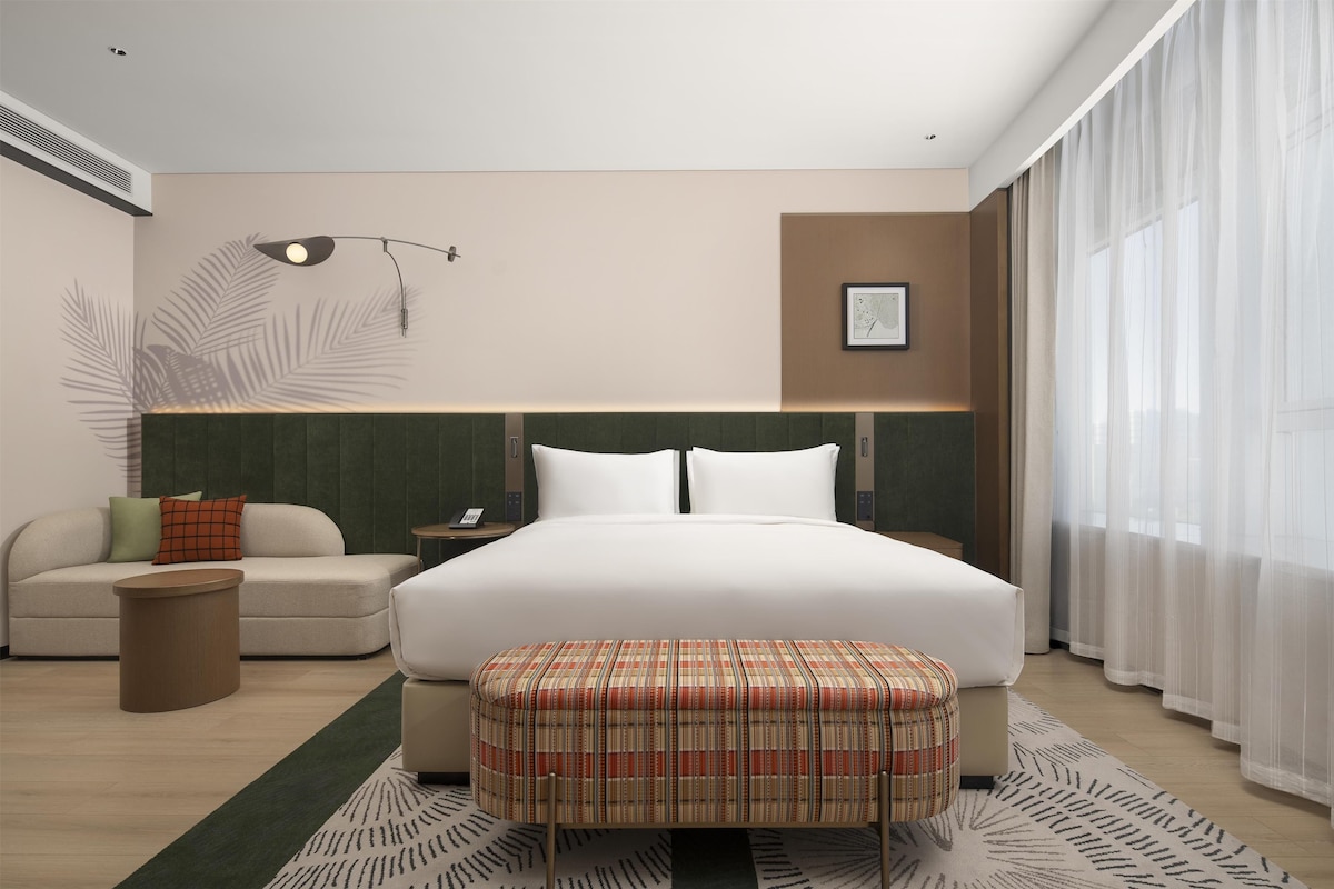 A hotel room with a bed, a sofa, a small table, a telephone, and a window with curtains.