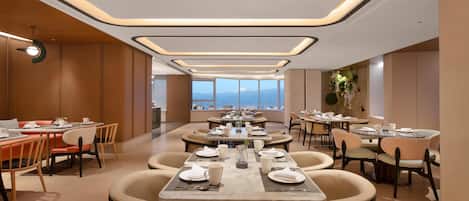 Un comedor moderno con mesas dispuestas para comidas, vista a las montañas y un diseño de techo único.