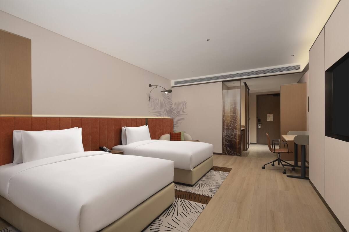 A modern hotel room with two beds, a desk, and a chair.