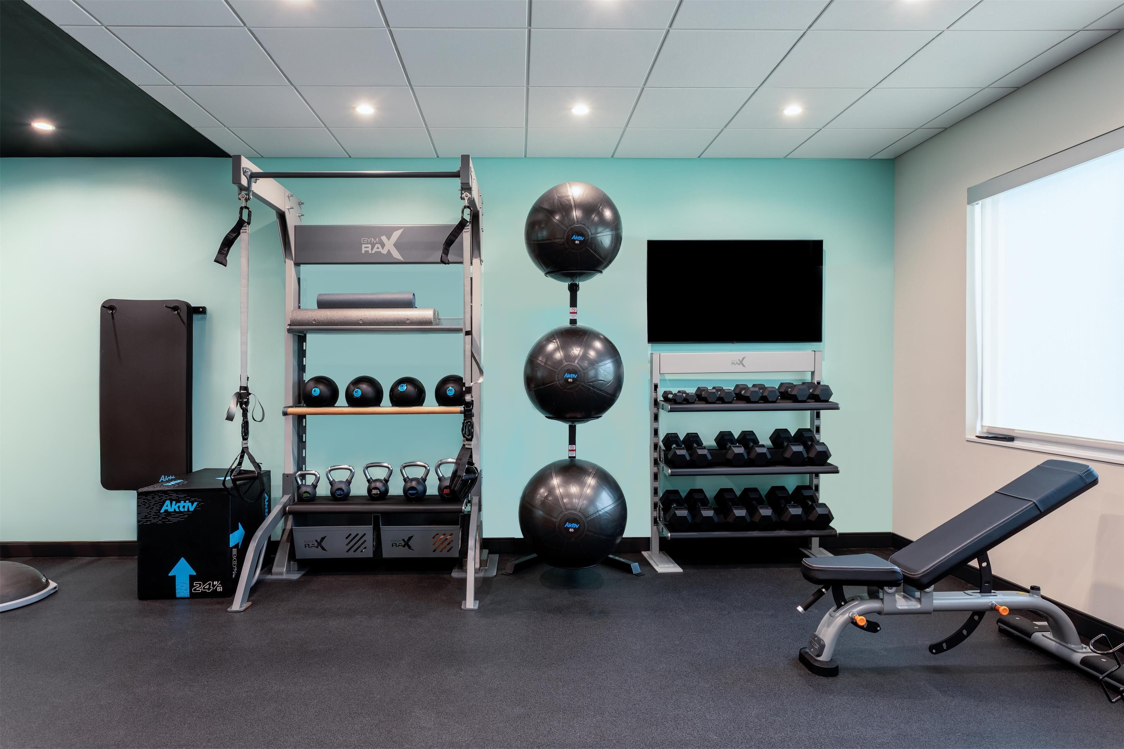 Un gimnasio con barra de dominadas, kettelbells, mancuernas y un banco.