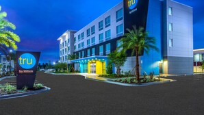 Un moderno edificio de hotel con un llamativo letrero 'tru by Hilton', varios pisos y una entrada bien iluminada.