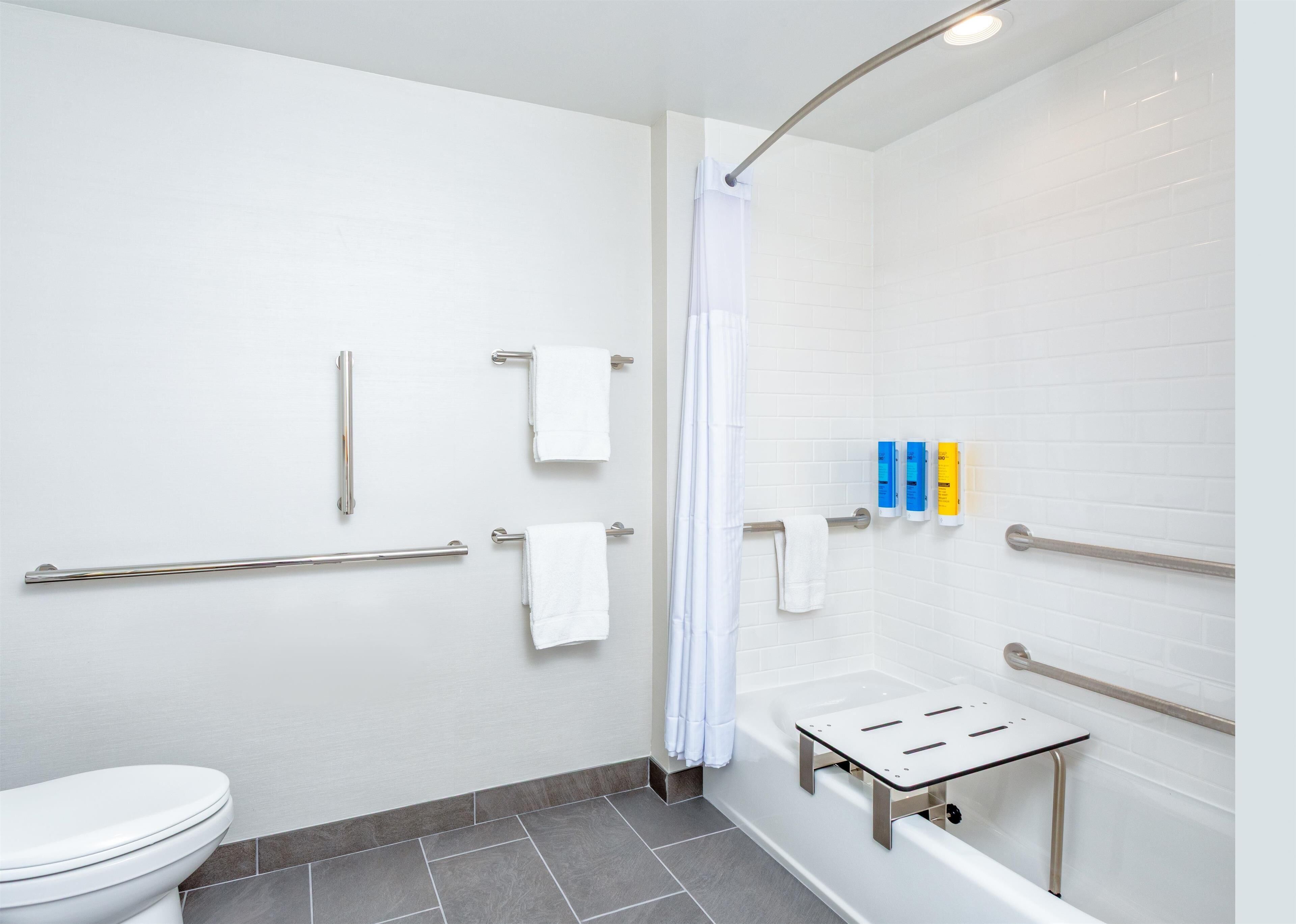 Et moderne badeværelse med hvide fliser, en bruseniche med buet glasdør, toilet og gelænder i nærheden af bruseren.