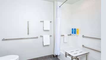 A modern bathroom with white tiles, a shower with a curved glass door, a toilet, and a grab bar near the shower.