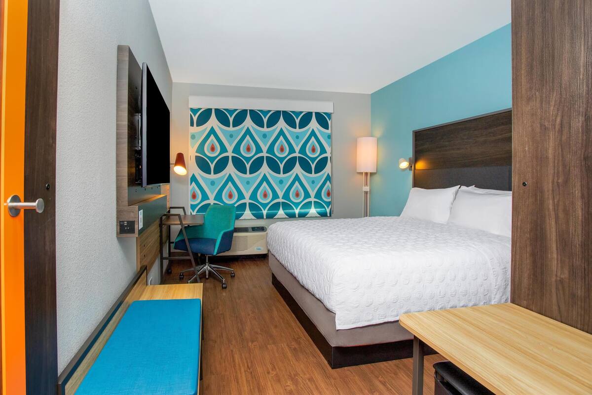 A hotel room with a bed, desk, chair, and a TV mounted on the wall.