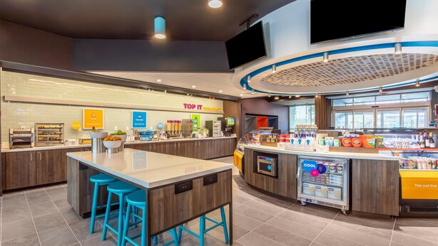 Una cafetería moderna con una isla central, taburetes de bar, un expositor refrigerado y un letrero que dice 'Top It'.