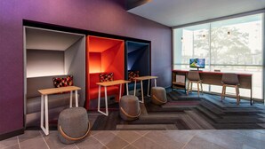 Un espacio de oficina moderno con una zona de estar en rojo y azul, un escritorio con computadora y un amplio ventanal con vistas al exterior.