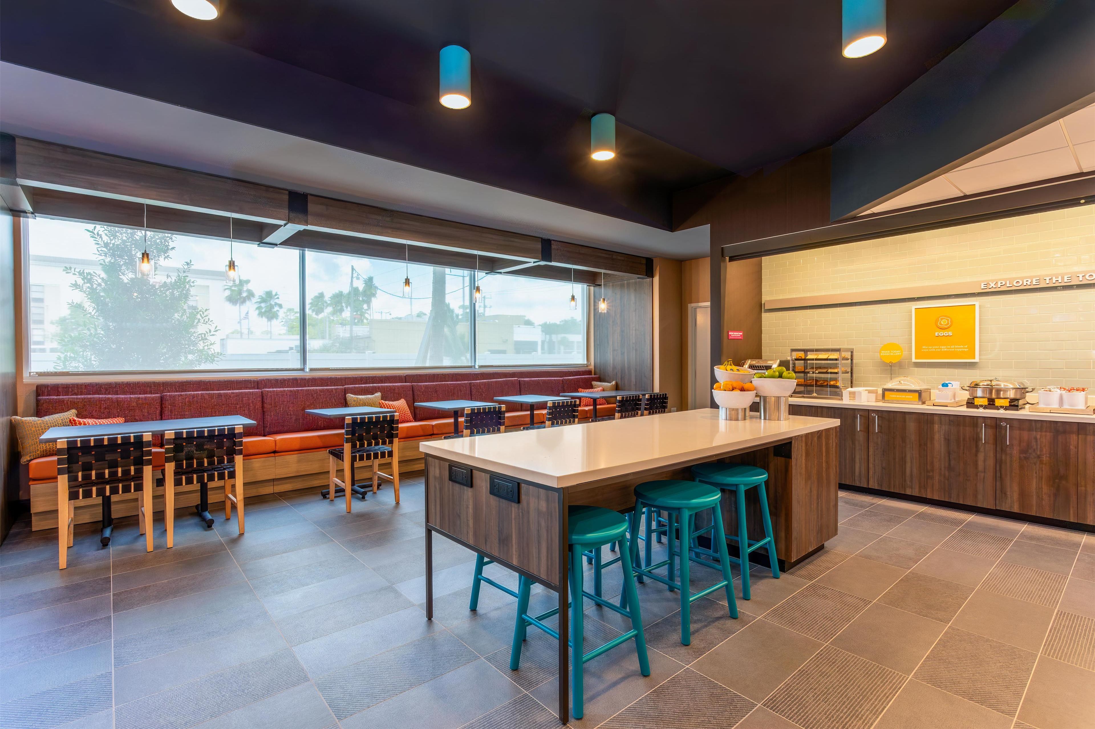 A modern restaurant with a long communal table, bar stools, and a seating area with benches.