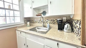 A kitchen with white cabinets, a stainless steel sink, a coffee maker, and a toaster. - Coastal Cottage 225 - Walk to Beach, King Bed (Cocoa Beach)