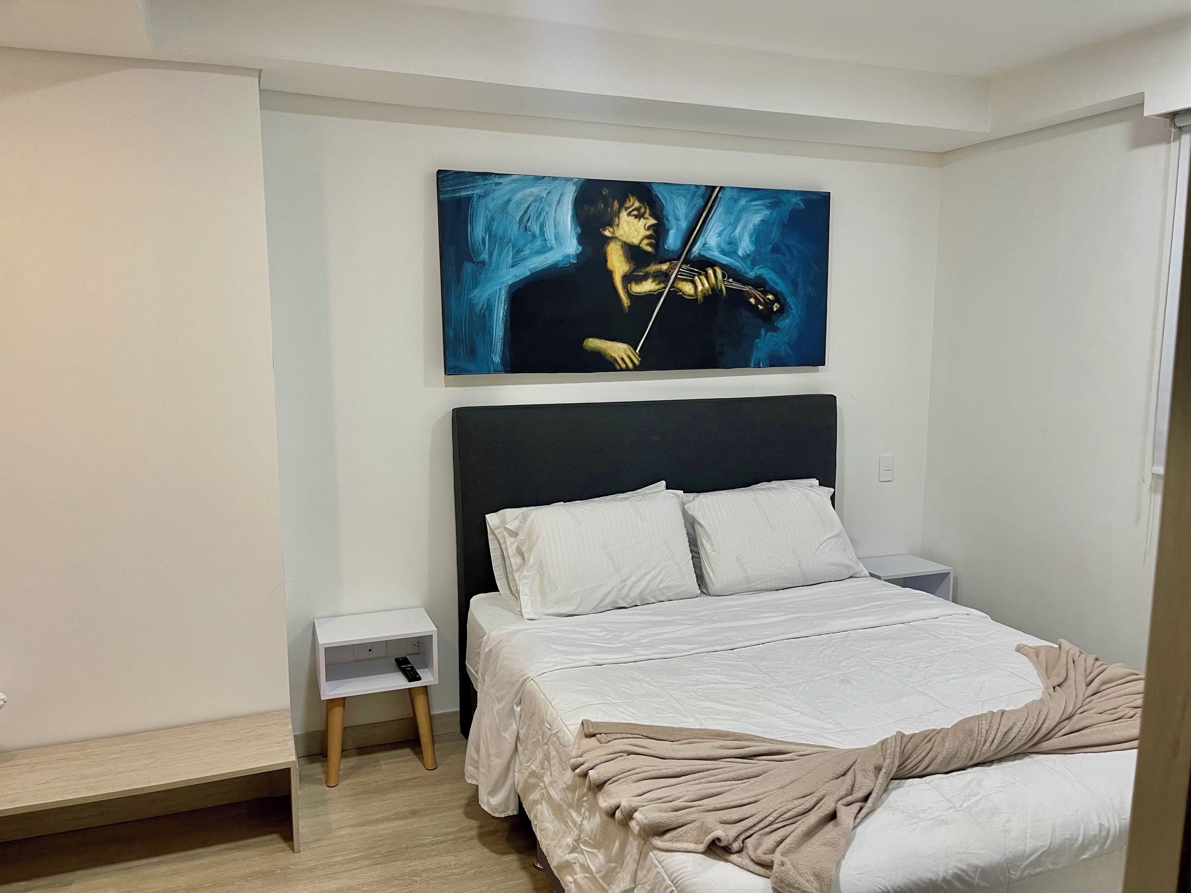 Un dormitorio con cama, una mesita de noche, un cuadro en la pared y suelo de madera.