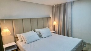 A neatly made bed with white bedding and pillows, a bedside table with a lamp, and a headboard.