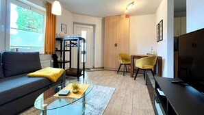 Un salon moderne avec un canapé, une table basse en verre et un téléviseur. Il y a également un coin repas avec une table et des chaises.