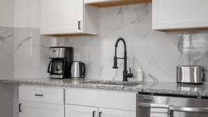 Una cocina moderna con armarios blancos, protector contra salpicaduras de mármol, cafetera, tostadora y lavavajillas.