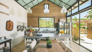 A modern kitchen with a large island, pendant lights, and a view of the garden.