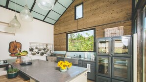 A modern kitchen with a large island, stainless steel appliances, and a view of greenery outside.