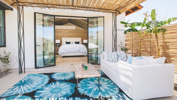 A modern bedroom with a bed, a white sofa, and a glass door leading to a balcony.