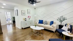 Un salon moderne avec un canapé blanc, des coussins bleus, une table basse et un meuble blanc agrémenté d’objets décoratifs.
