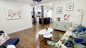 Un salon moderne avec un plancher en bois, une table ronde blanche, un canapé bleu et un meuble blanc orné de motifs géométriques.