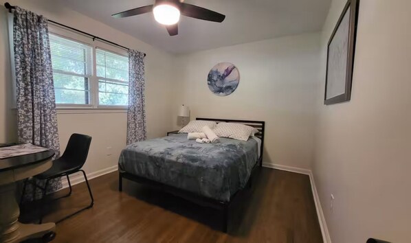 A bedroom with a bed, a desk, a chair, a ceiling fan, a window with curtains, and a wall-mounted picture. - Charming 4-bedroom house Old Town Lilburn (Lilburn)