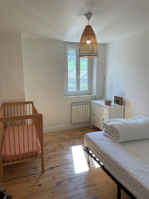 A bedroom with a crib, a bed, a radiator, a window, and a hanging light fixture. - Charming country house, quiet garden with trees, near Lake Paladru (Valencogne)