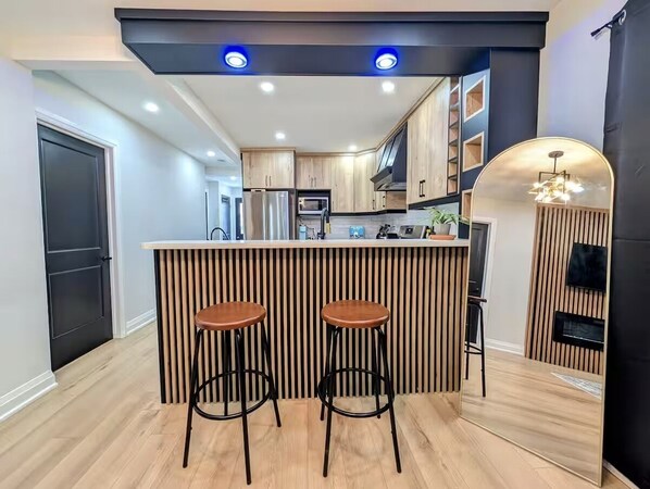 Una cocina moderna con una isla central, dos taburetes y electrodomésticos integrados.