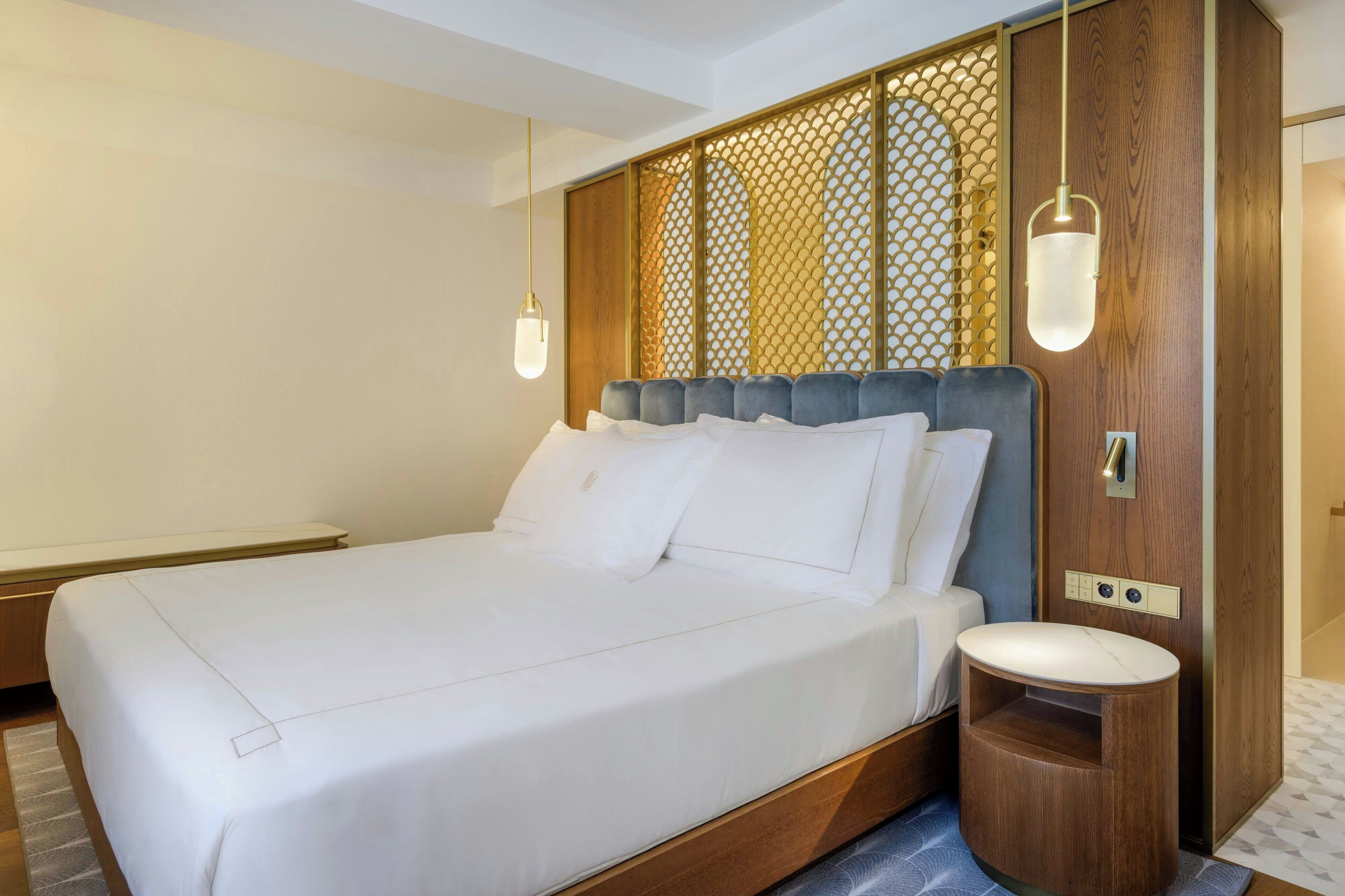 A neatly made bed with white linens, a wooden headboard, and a bedside table with a white lamp.