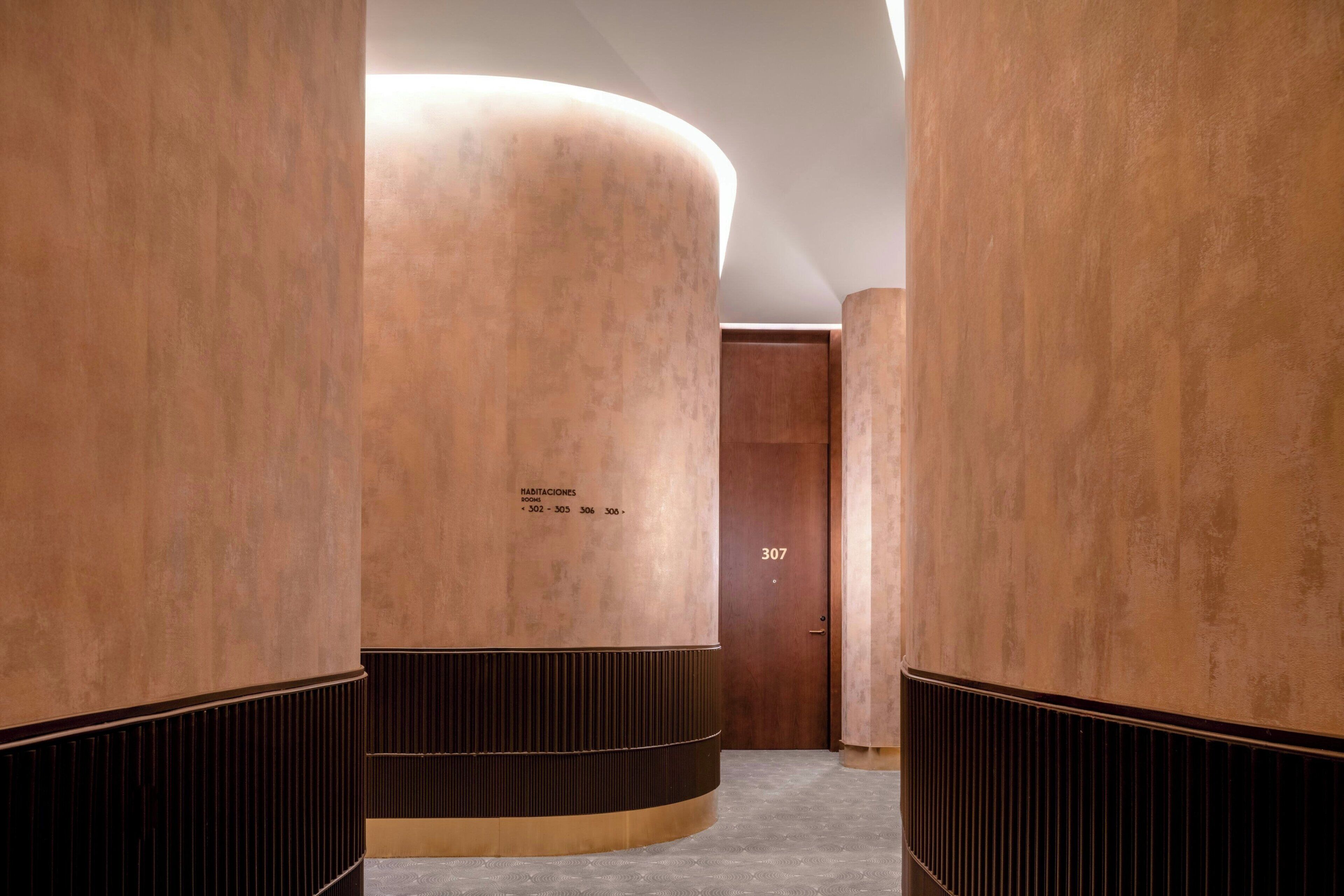 A hallway with large cylindrical columns, a wooden door labeled "307", and a textured floor.