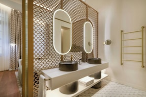 Un baño moderno con un tocador blanco, dos lavabos redondos y un espejo grande con iluminación integrada.