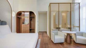 A hotel room with a bed, a wooden wardrobe, a seating area with two chairs and a table, and a large window.