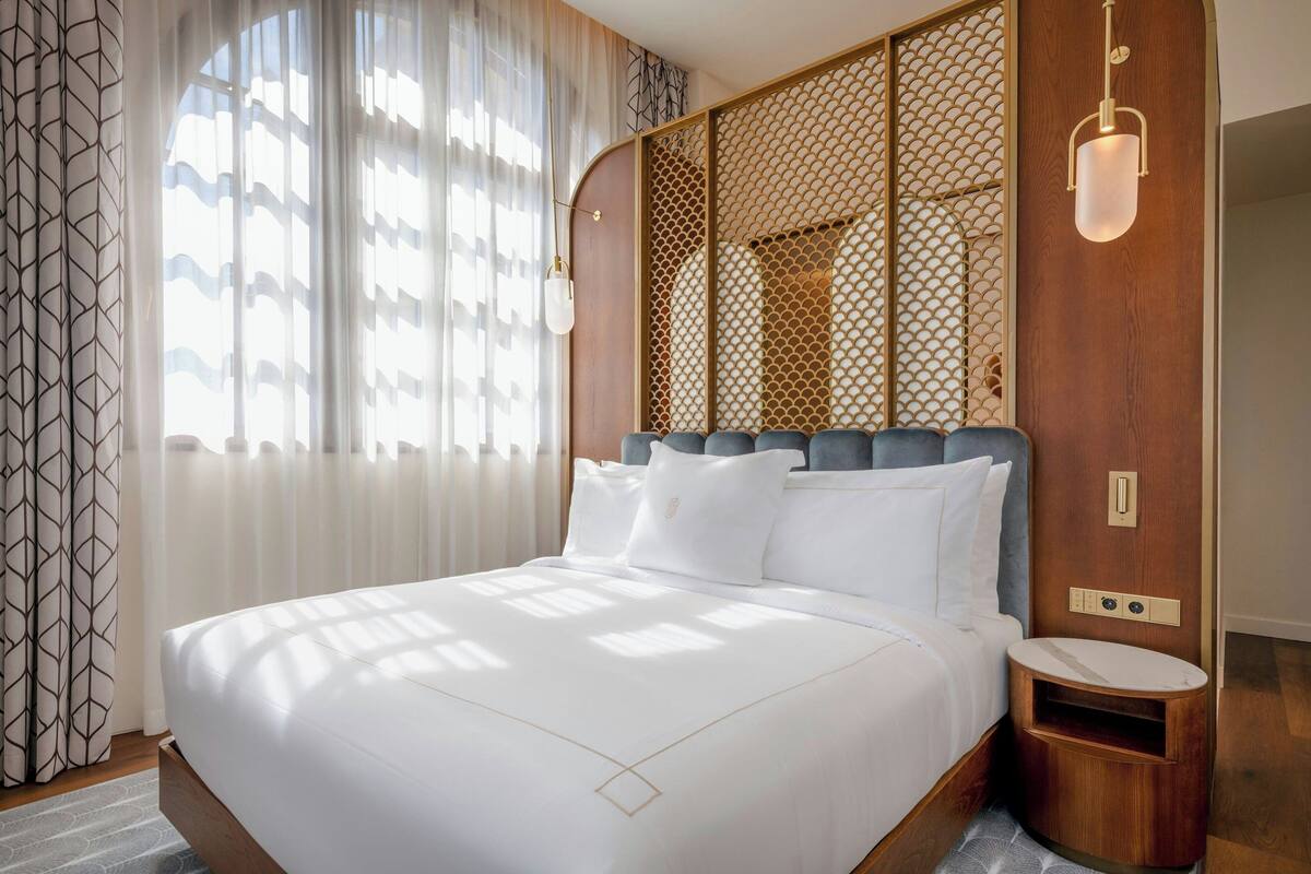 A neatly made bed with white linens, a wooden headboard, and a bedside table with a lamp.
