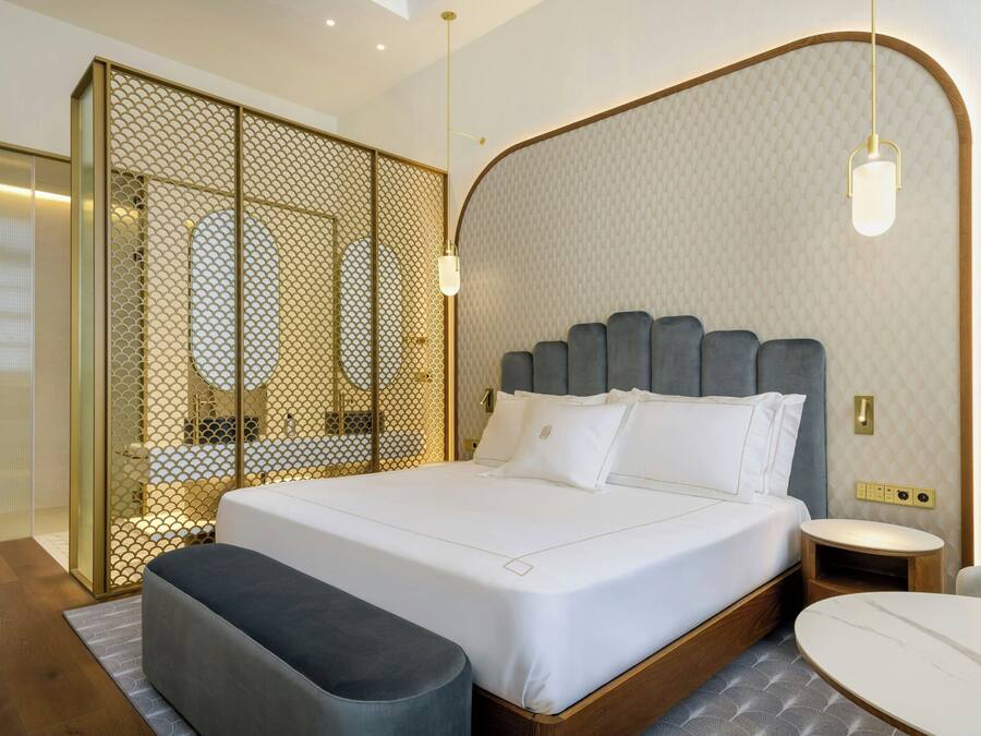 A modern bedroom with a large bed, bedside tables, a bench, and a small table.