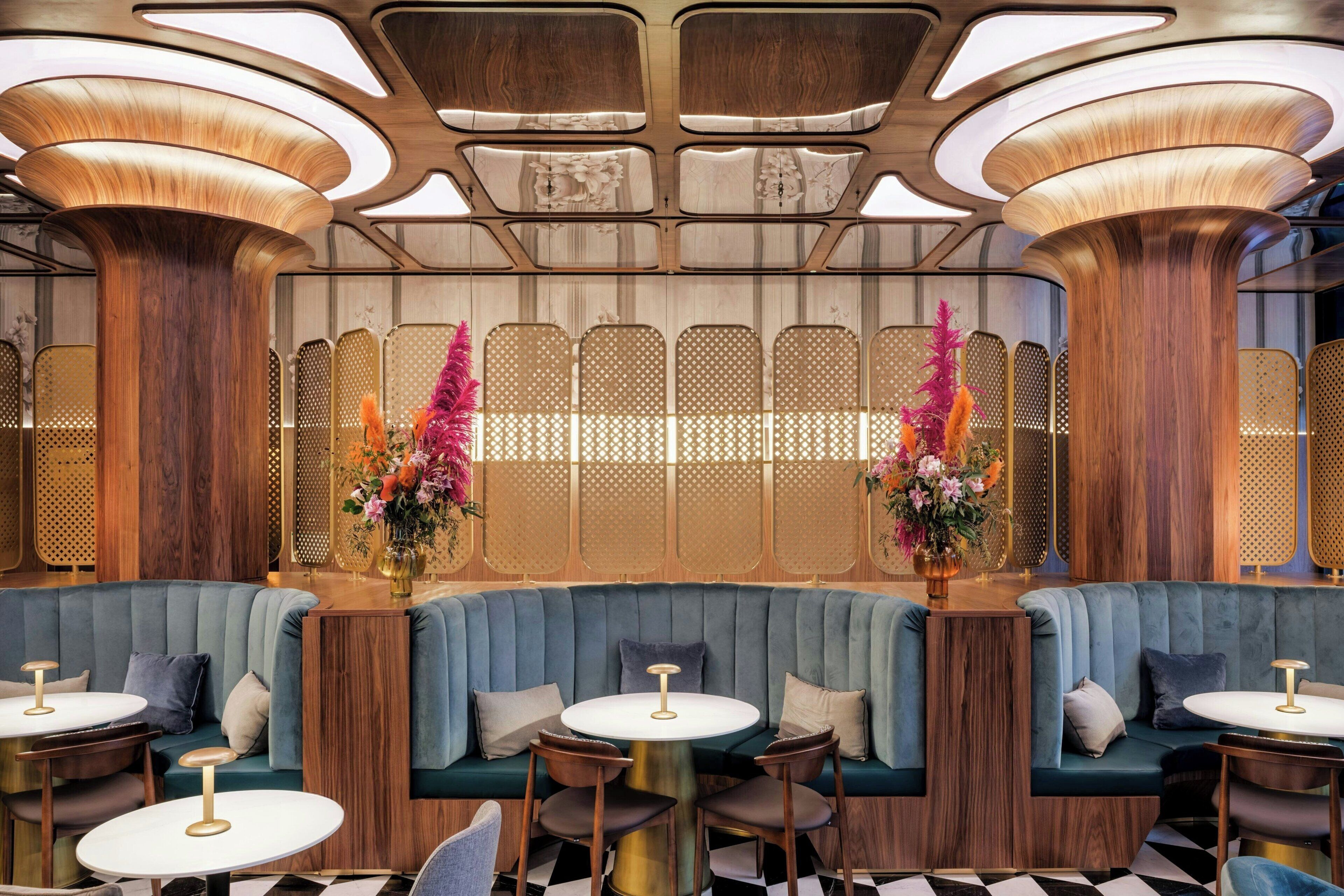 Un intérieur moderne avec un banc recouvert d’un tissu bleu, des tables rondes et des compositions florales décoratives.