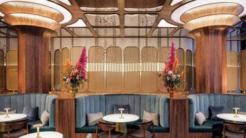Un intérieur moderne avec un banc recouvert d’un tissu bleu, des tables rondes et des compositions florales décoratives.