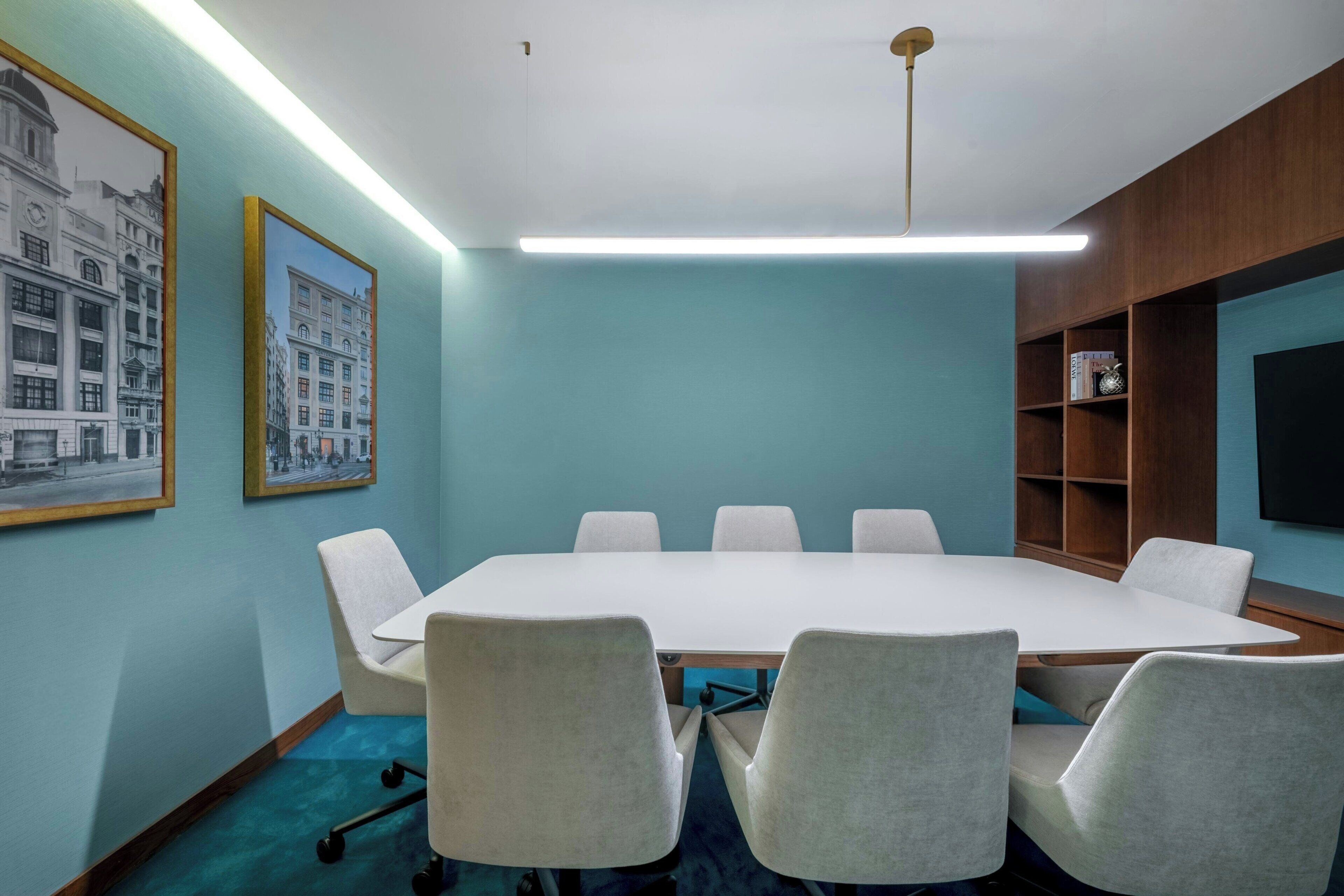 Un salón de conferencias con una larga mesa y seis sillas, paredes color esmeralda y cuadros en la pared.