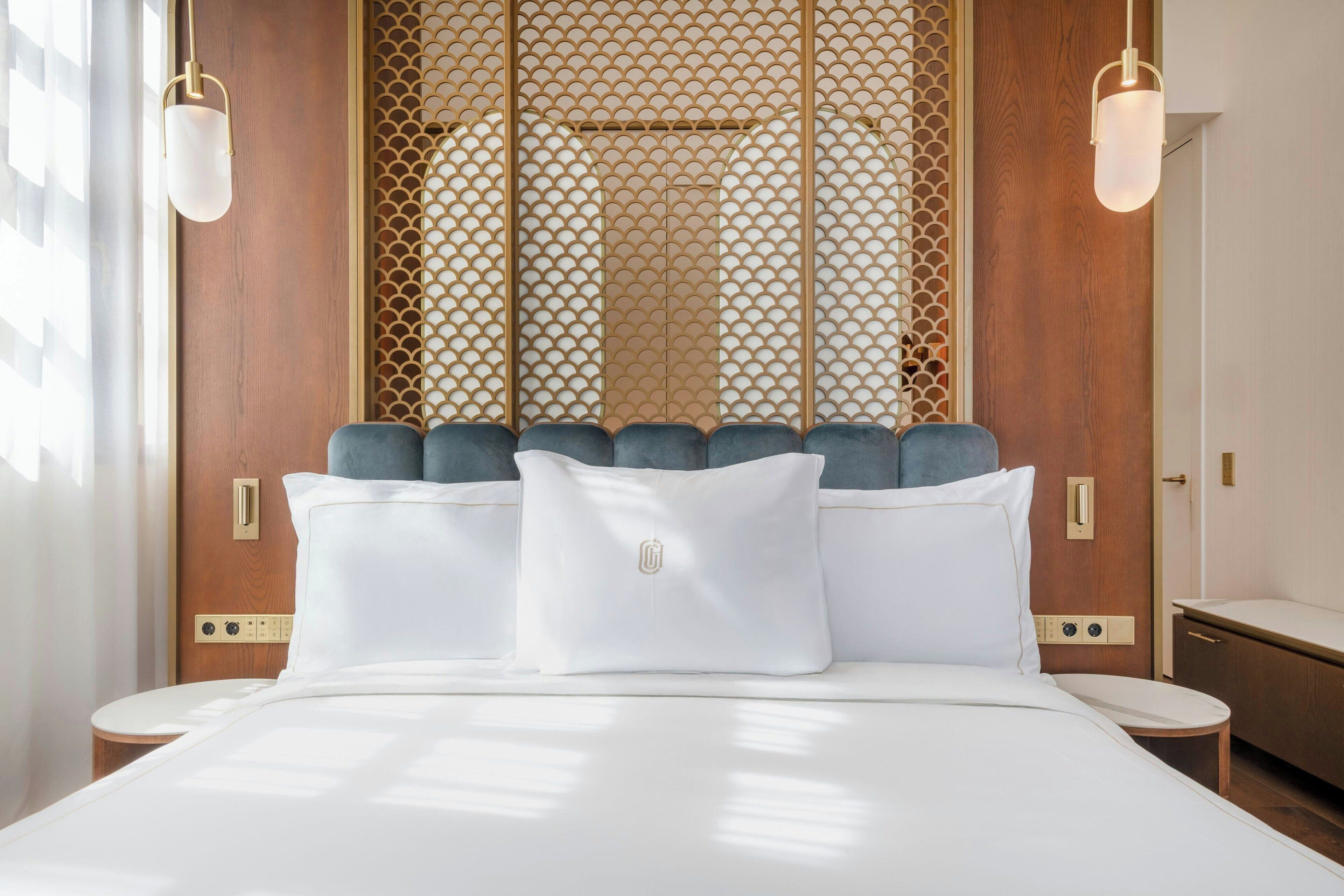 Een hotelkamer met een bed, een nachtkastje, een houten hoofdeinde en een decoratief scherm.