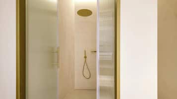 A narrow, glass-walled walk-in shower with a gold showerhead and a ceiling-mounted circular light fixture.