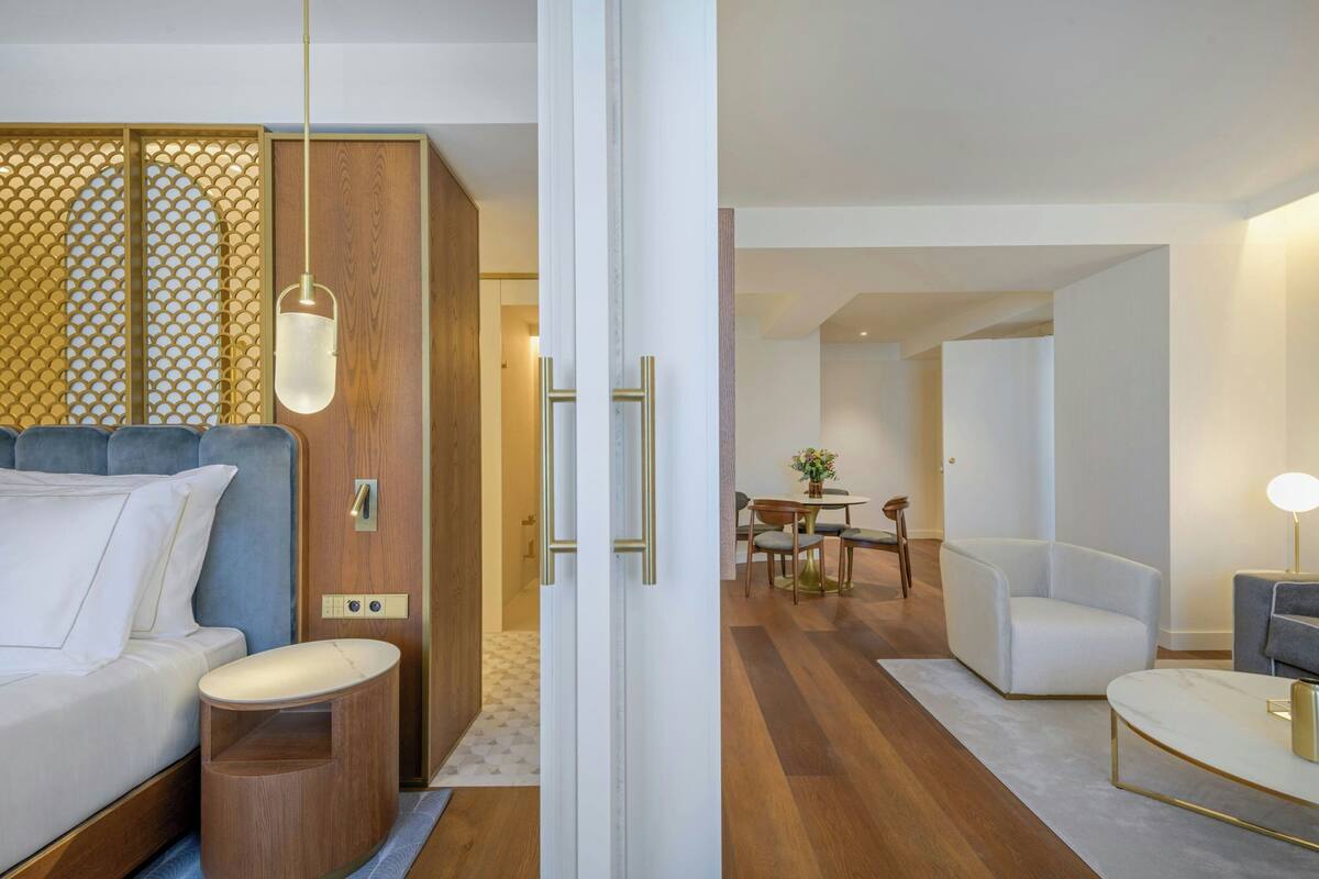 A modern hotel room with a bed, bedside table, and a wooden partition with a geometric pattern.