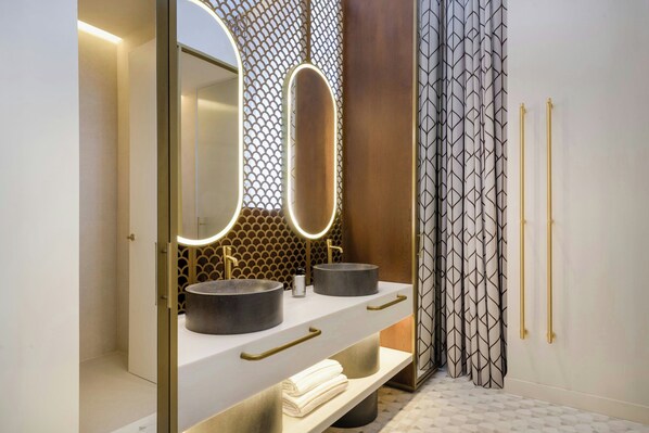 A modern bathroom with a double sink vanity, a large mirror with integrated lighting, and a decorative wall panel. - Grand Hotel Centenari, Valencia, Autograph Collection (Valencia)