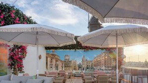 An outdoor seating area with white umbrellas, wicker chairs, and a mural of a cityscape. - Grand Hotel Centenari, Valencia, Autograph Collection (Valencia)
