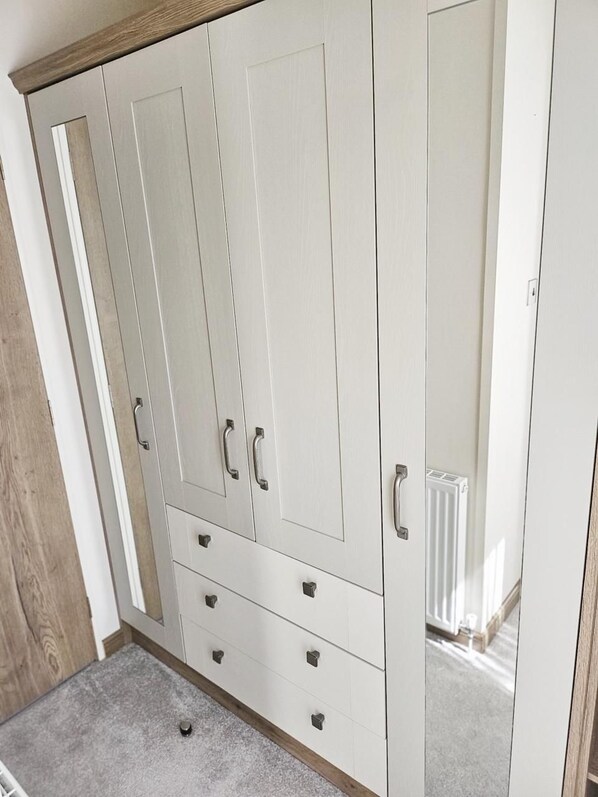 A white wardrobe with multiple doors and drawers, a wooden floor, and a radiator in the background.