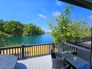 A deck with a table and chairs overlooking a river, surrounded by trees and a wooden fence.