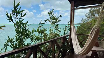 Una silla hamaca sobre una terraza de madera con vistas a aguas turquesas, con plantas de bambú al frente.