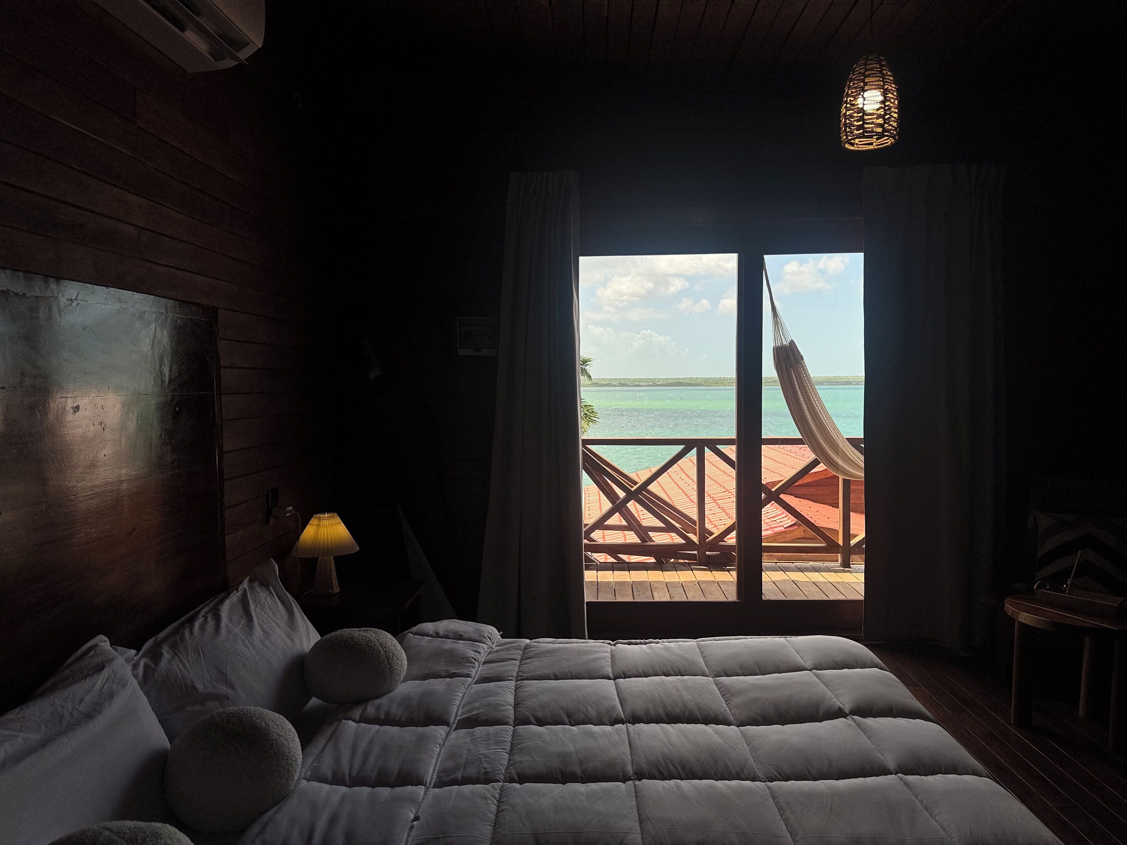 Ein Schlafzimmer mit einem großen Bett, einem Nachttisch, einer Lampe und Meerblick durch eine Schiebetür.