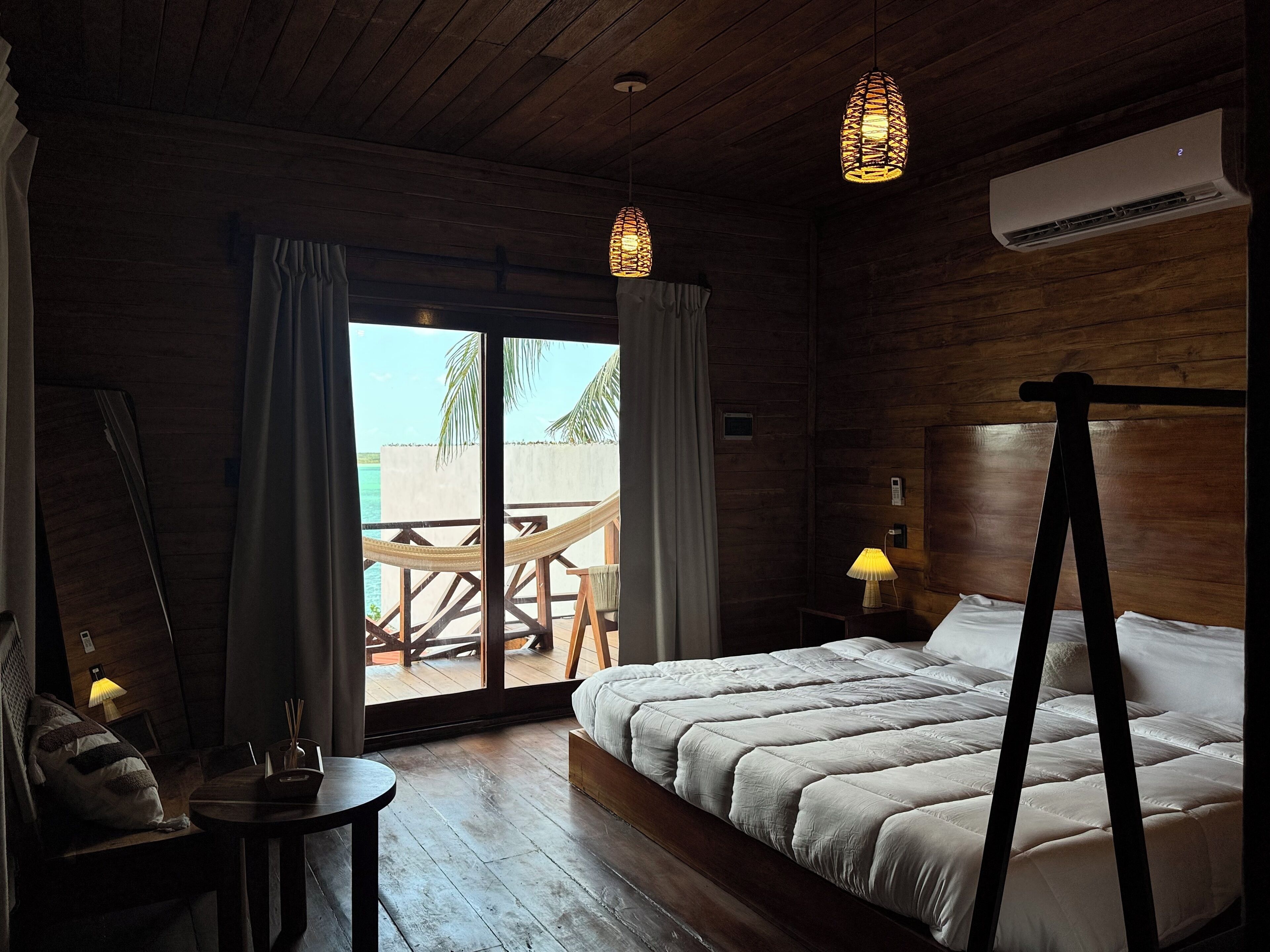 A wooden room with a bed, a table, and a view of the outdoors.