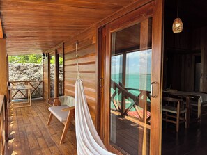 A wooden deck with a hammock, a table, and chairs, overlooking turquoise water. - Hotel Maria Isabel Bacalar (Bacalar)
